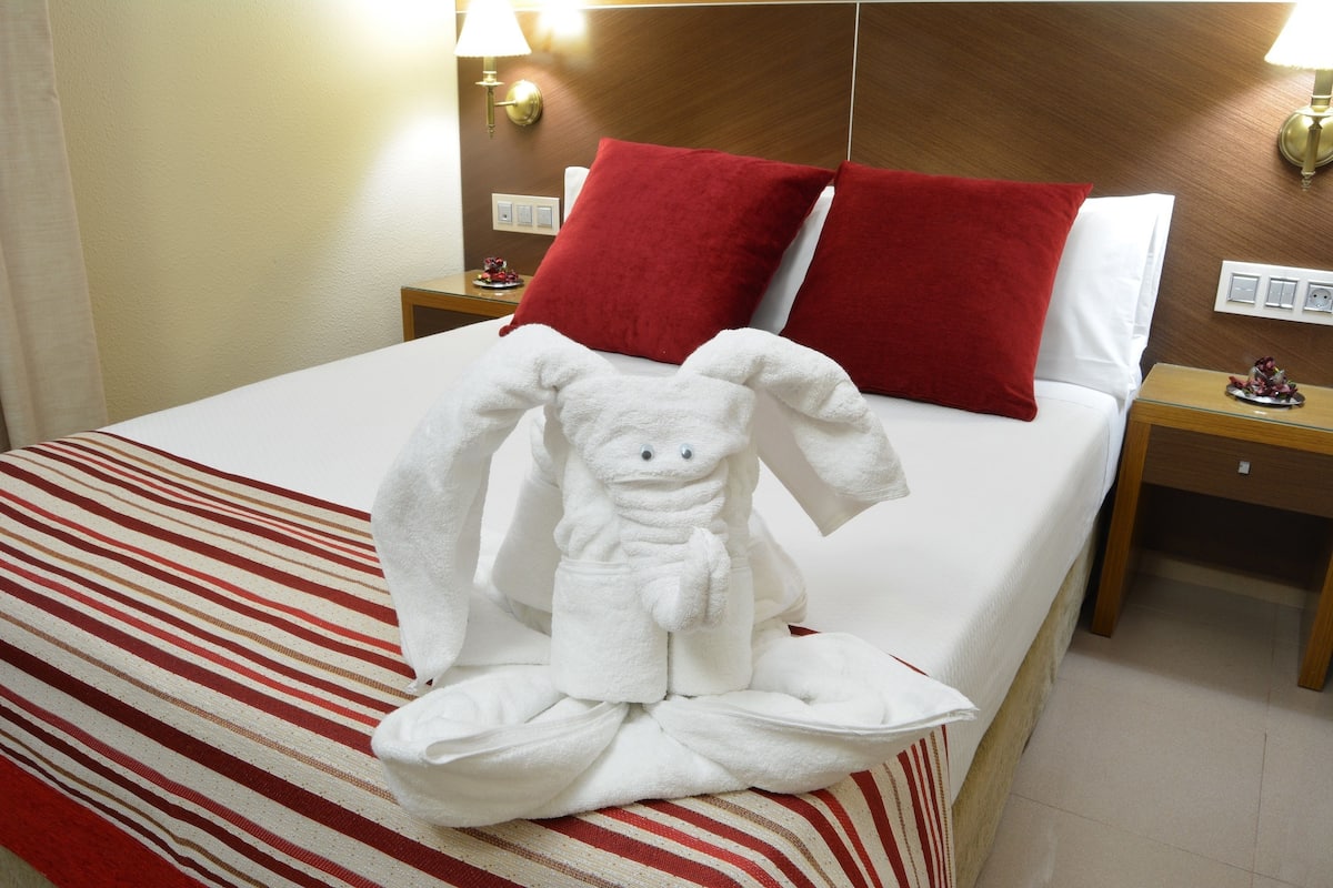 Ein Hotelzimmer mit einem ordentlich bezogenen Bett, einer roten und weißen Streifenauflage und einer Tierform aus Handtüchern auf dem Bett.