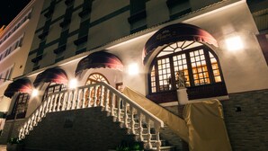 Un edificio con una escalera que conduce a un nivel superior, un balcón con barandilla y un gran ventanal con vista al interior.