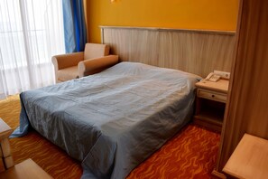A hotel room with a bed, a chair, a bedside table with a phone, and a window with curtains. - Brigantina Beach (Varna)