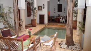 Un patio con piscina, mobiliario de mimbre y plantas en macetas.