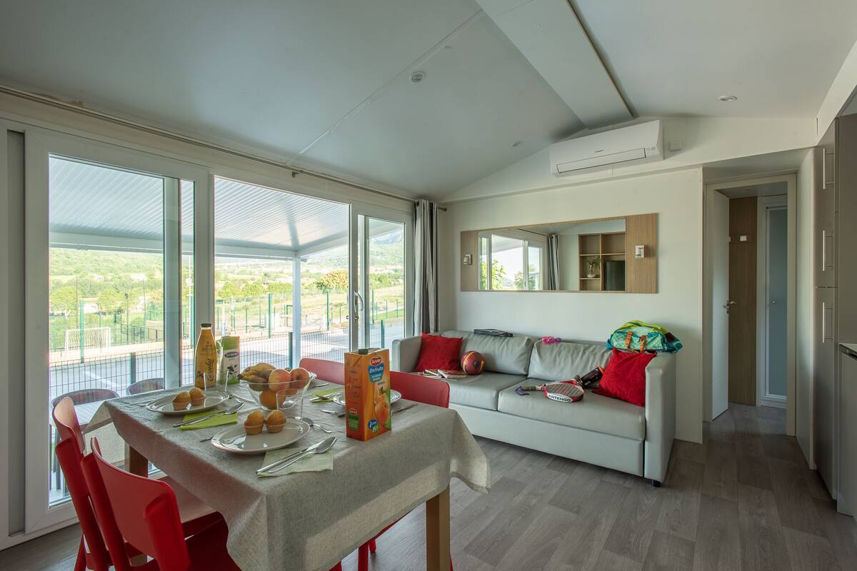 Uma sala de estar moderna com área de jantar, janelas amplas, um sofá e um espelho.