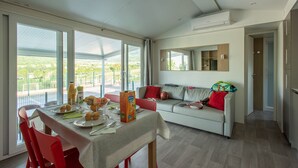 Una sala de estar moderna con comedor, ventanas amplias, un sofá y un espejo.