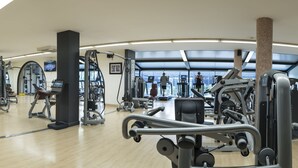 Un gimnasio con diferentes máquinas de ejercicio, un espejo y un ventanal grande.