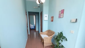 A hallway with a wicker chair and a potted plant, light blue walls, and a tiled floor. - Albergo Alba (Turin)