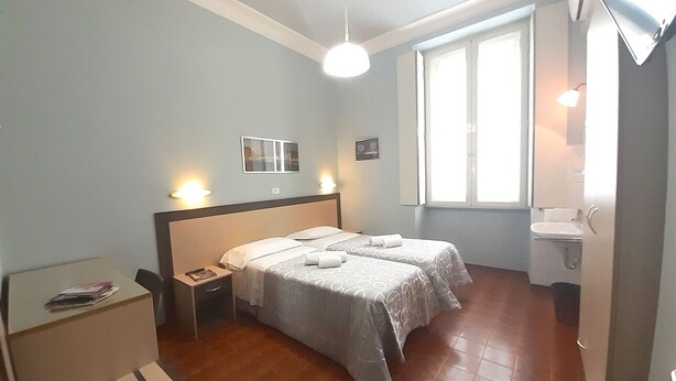 A bedroom with two beds, a desk, a chair, a window, and a bathroom. - Albergo Alba (Turin)
