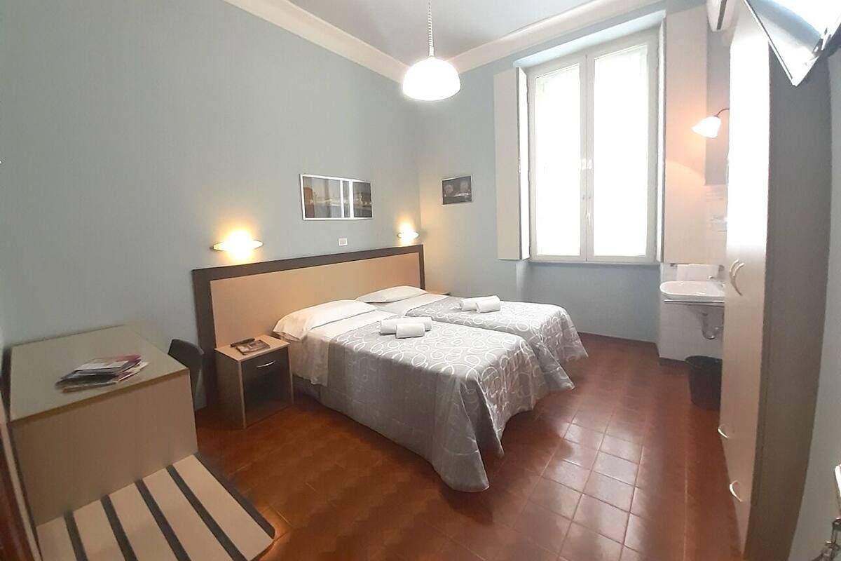 Un dormitorio con dos camas, un escritorio, una silla, una ventana y un baño.