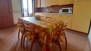 A kitchen with yellow cabinets, a microwave, and a dining table with chairs. - Albergo Alba (Turin)