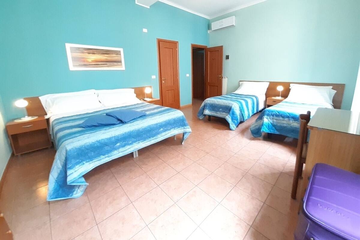 Una habitación con dos camas, una silla de madera, un mueble morado para guardar cosas y un aire acondicionado instalado en la pared.