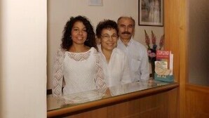 A reception area with a wooden counter, a framed picture on the wall, and a small decorative item on the counter. - Albergo Alba (Turin)