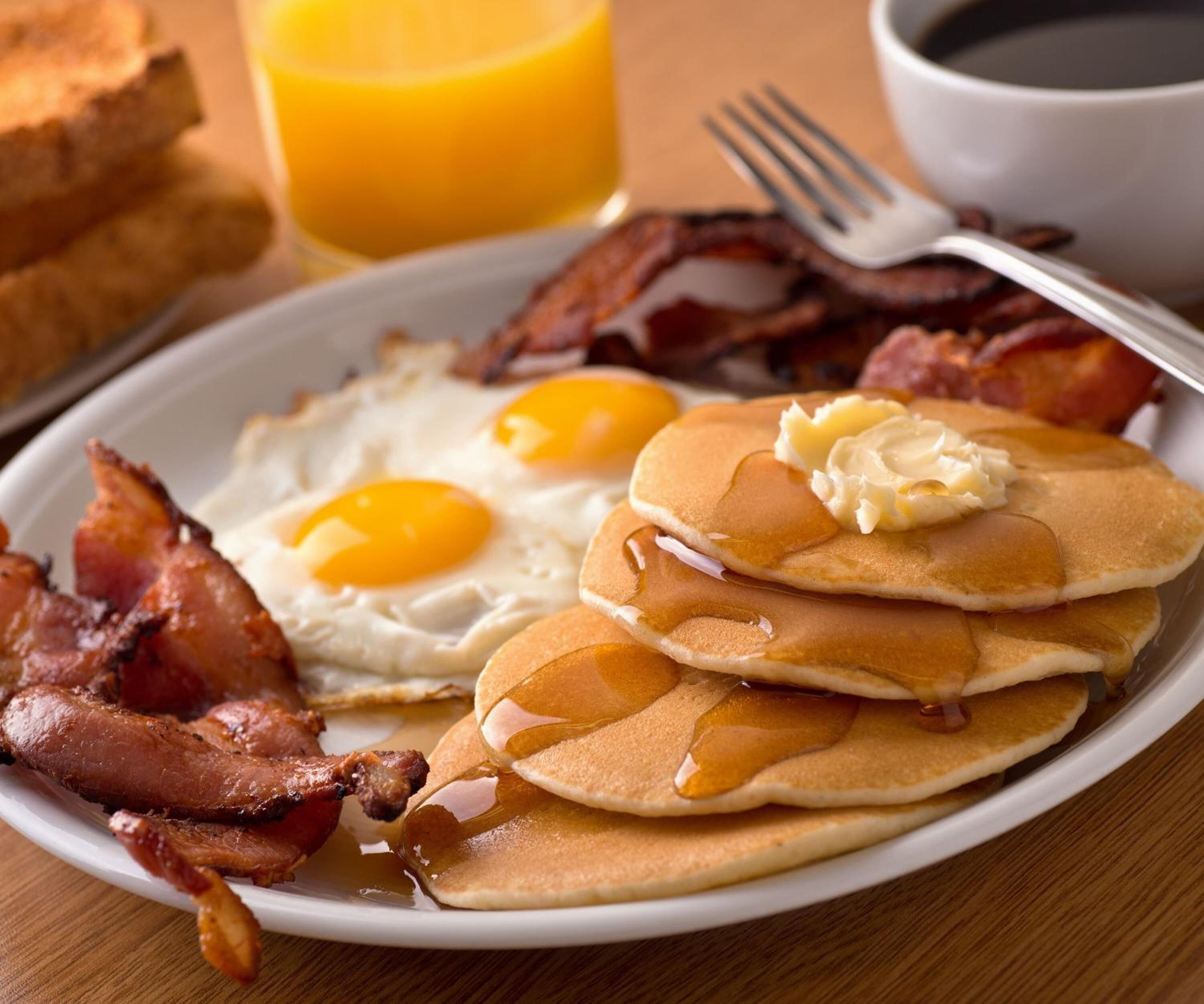A breakfast plate with eggs, bacon, pancakes, and butter.