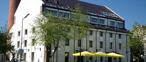 A hotel with a modern design, featuring a prominent chimney, large windows, and outdoor seating with yellow umbrellas.