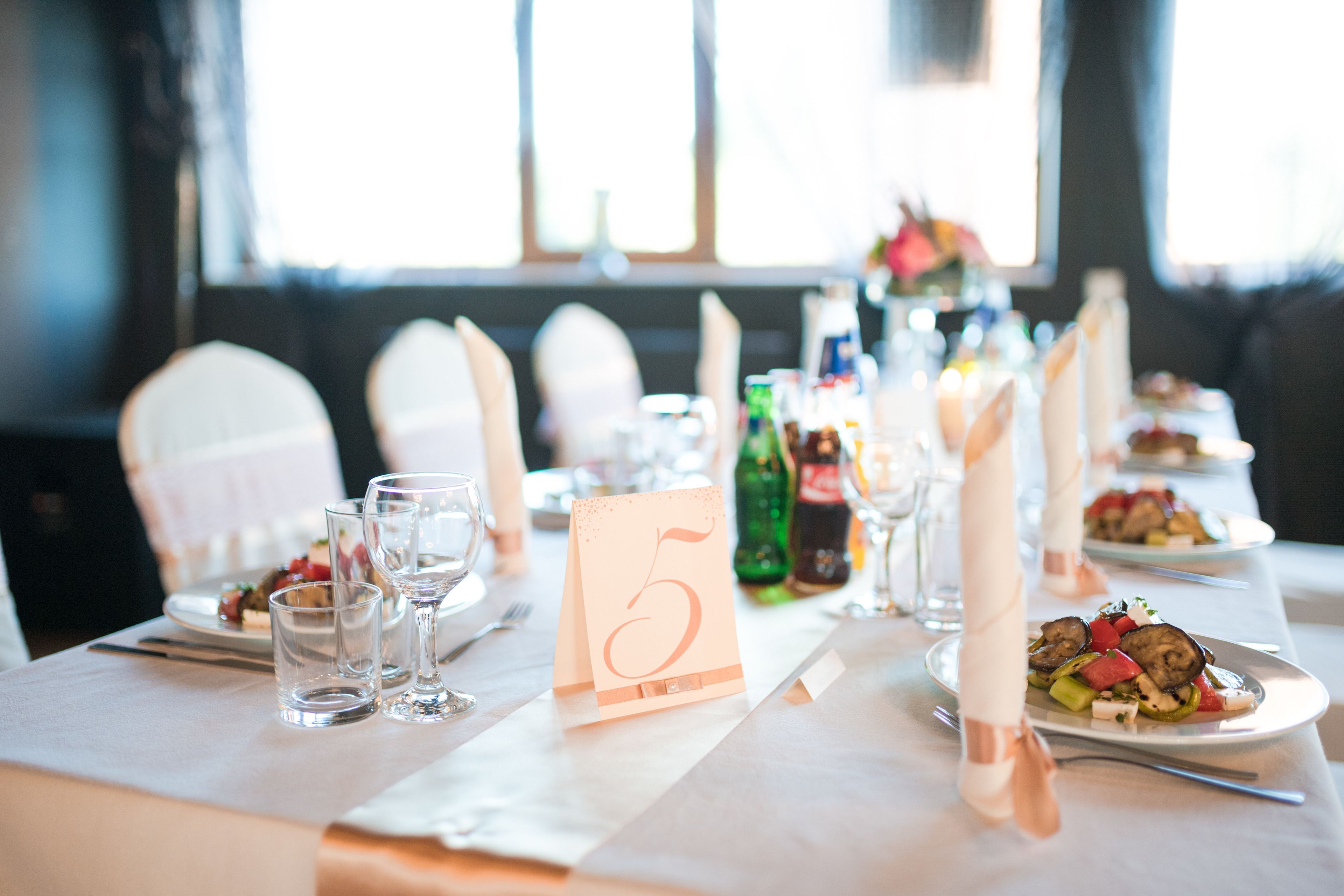 Una mesa de comedor dispuesta con tarjetas de lugar numeradas, vasos y platos con comida.