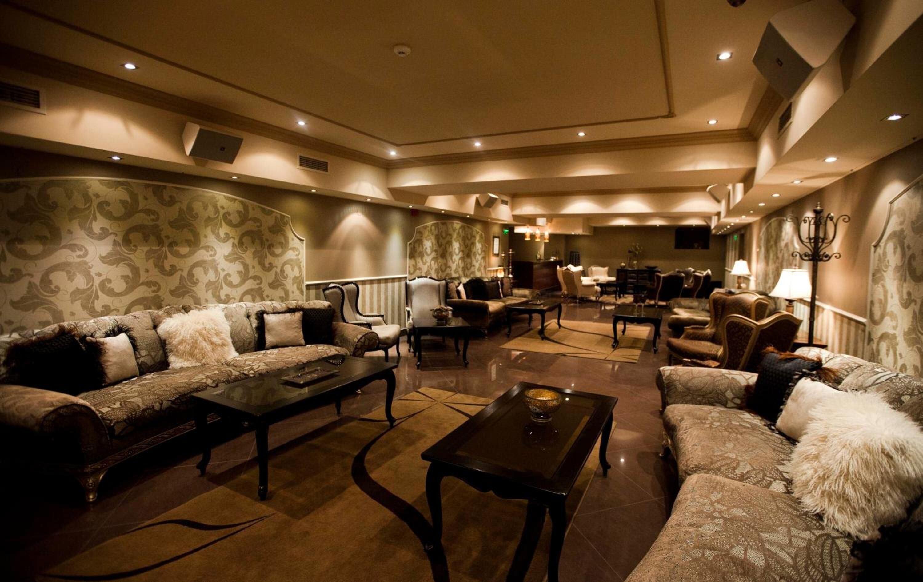En rummelig lounge med tapet, bløde sofaer og varierede siddepladser, herunder lænestole og et sofabord.