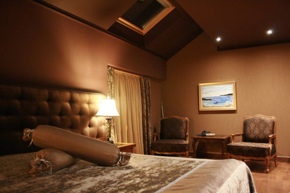A hotel room with a large bed, two armchairs, a small table, a lamp, and a painting on the wall.
