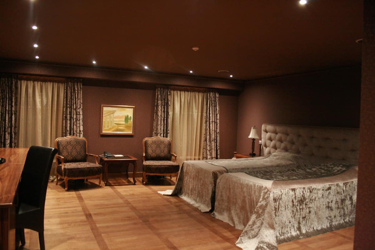 A hotel room with a large bed, two armchairs, a small table, and a desk.