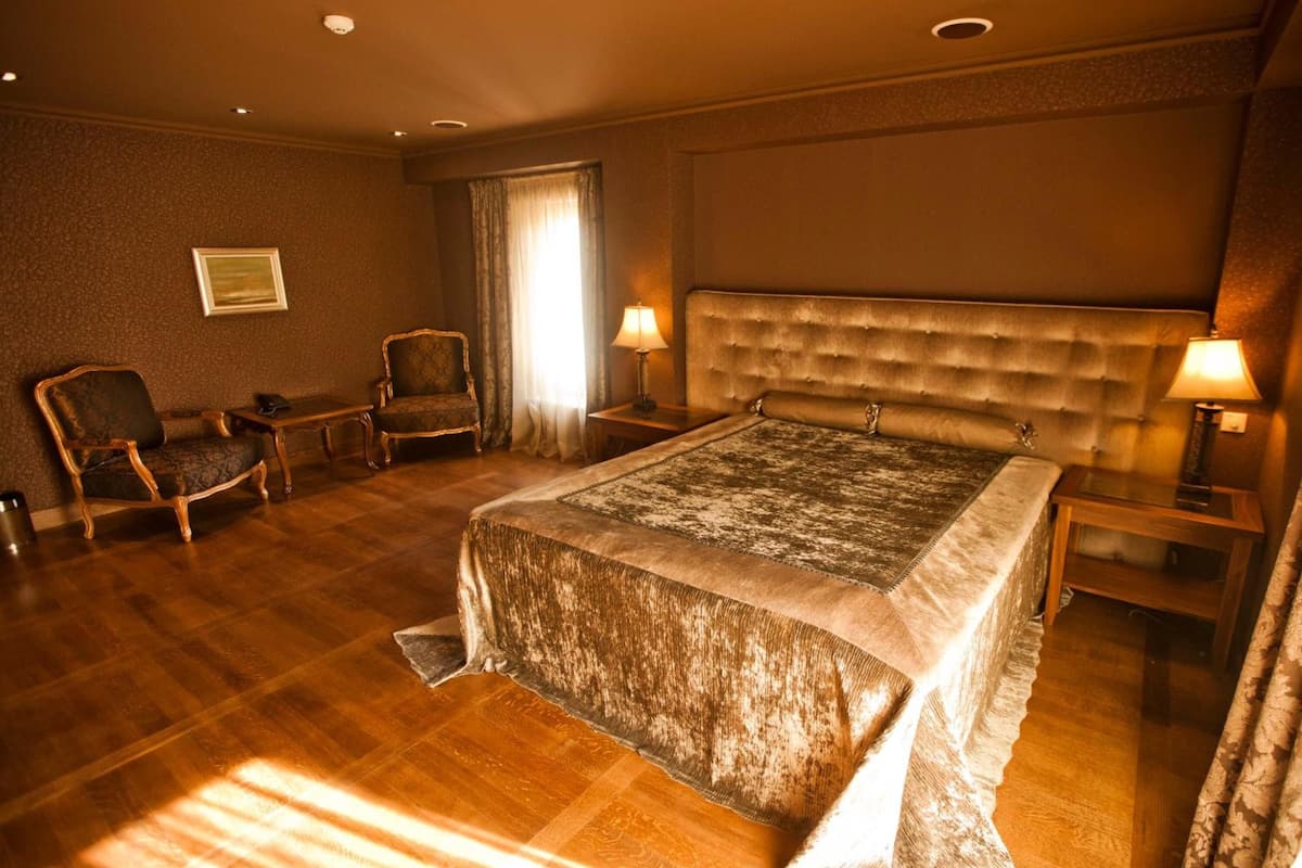 A hotel room with a large bed, two armchairs, a small table, and a nightstand.