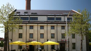 Un hotel de estilo arquitectónico clásico, con una entrada central, múltiples ventanas y asientos exteriores con sombrillas amarillas.