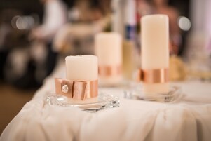 Una mesa con tres velas en soportes de vidrio transparente, cada una con una vela blanca y una banda dorada rosa.