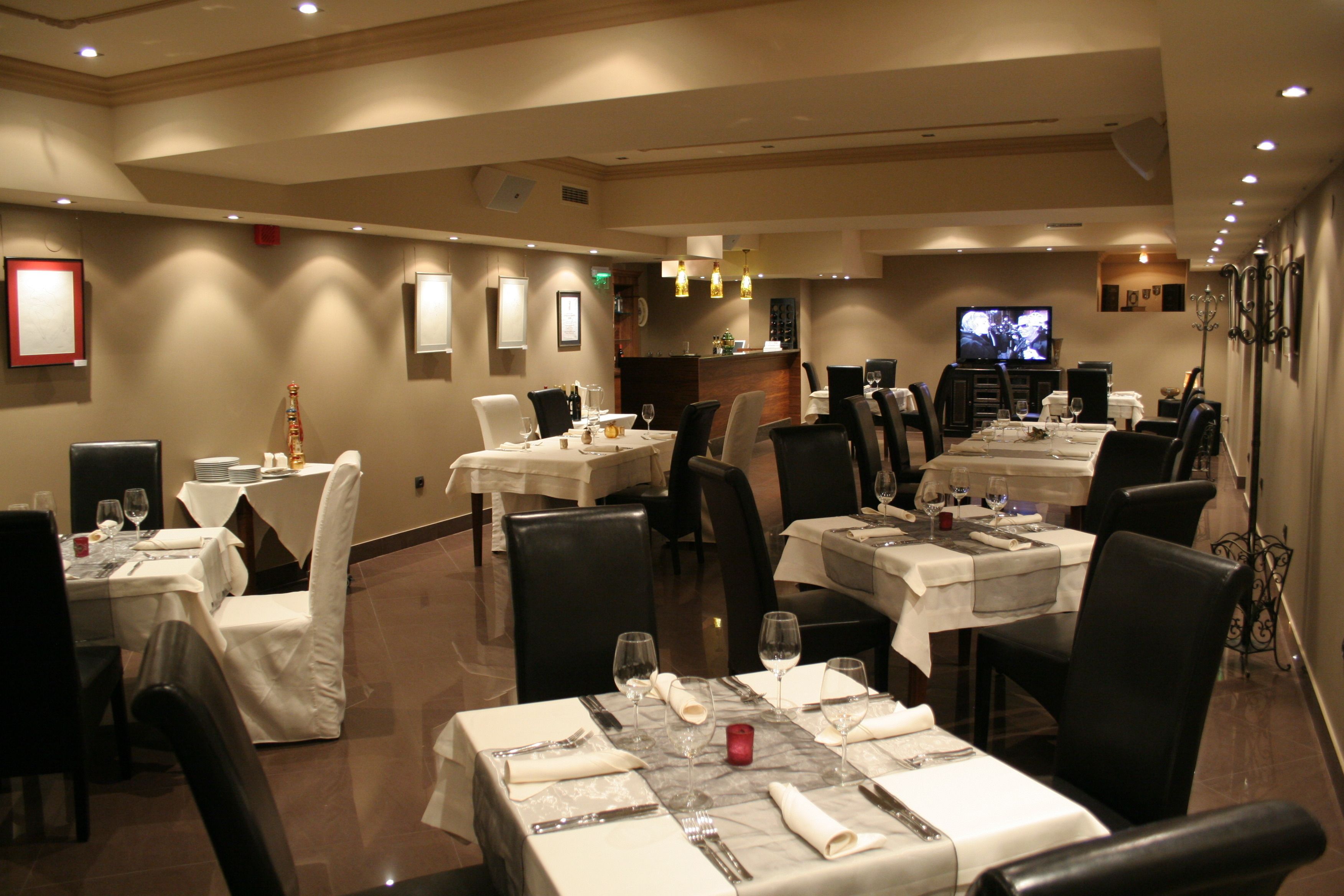Un restaurante con varias mesas dispuestas para comer, una zona de bar y una pantalla de televisión.