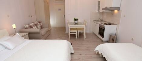 A hotel room with two beds, a dining table with chairs, a kitchenette, and a separate bathroom.