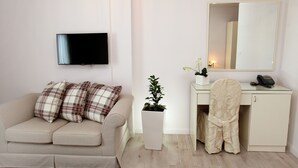 Una sala moderna con sofá, televisor de pantalla plana, escritorio con silla, planta en maceta y espejo.