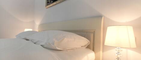 A neatly made bed with white linens and pillows, a bedside lamp, and a framed picture on the wall.