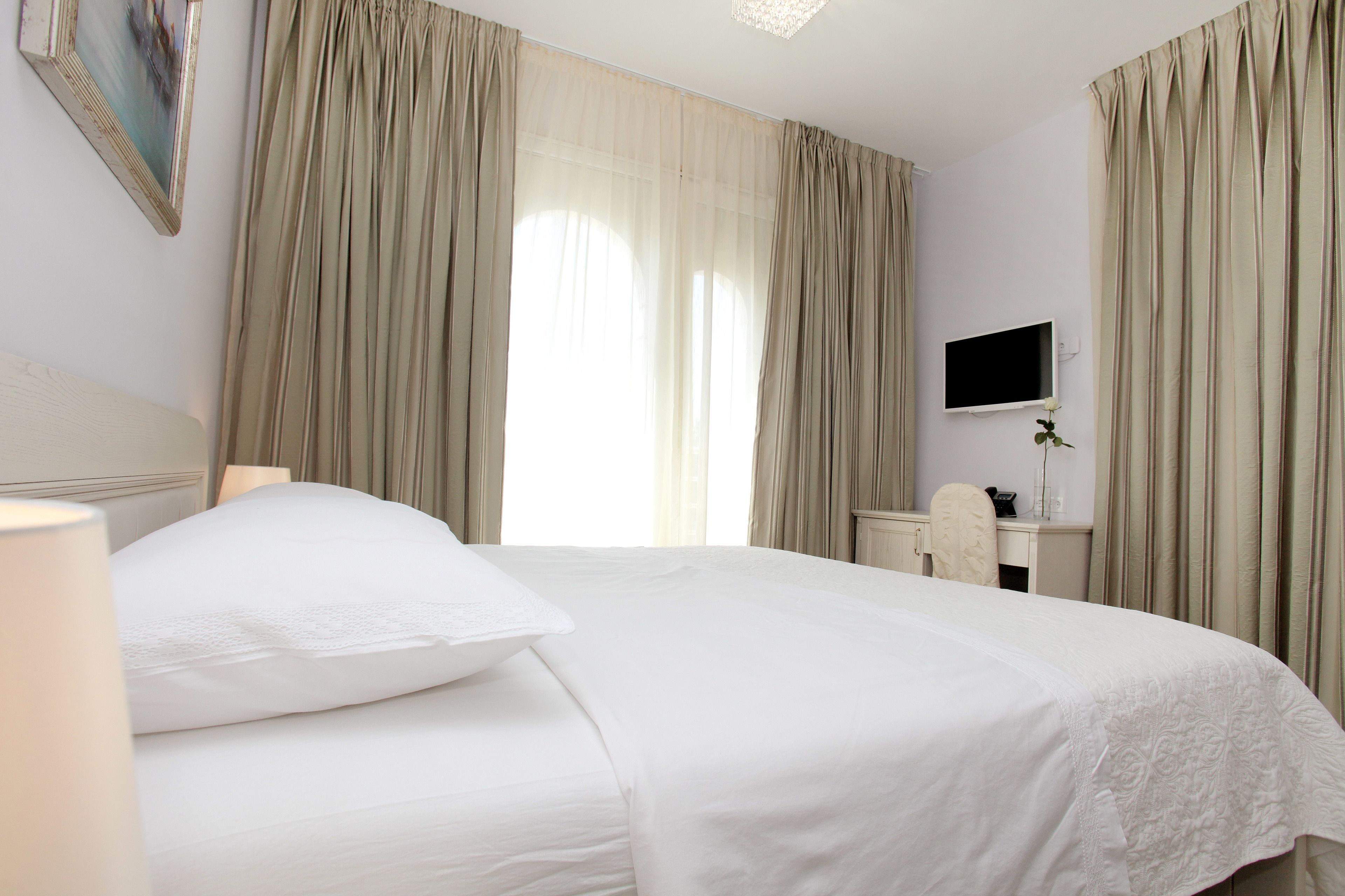 Una habitación de hotel con cama, escritorio, silla, televisor y cortinas.