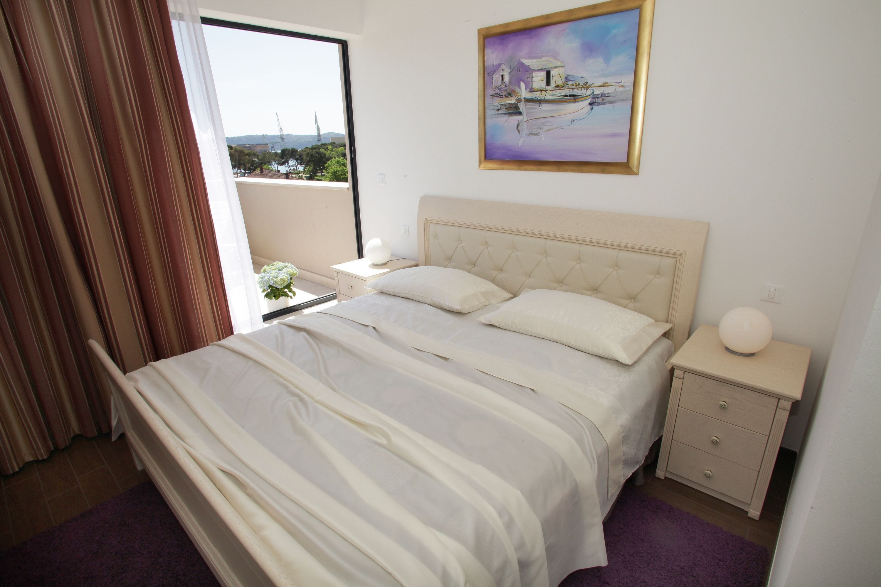 Ein Schlafzimmer mit Bett, Nachttisch, einem Fenster mit Vorhängen und einem Bild an der Wand.