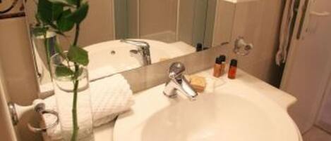 Une salle de bain avec un lavabo blanc, un miroir, un vase contenant une rose blanche et des articles de toilette.