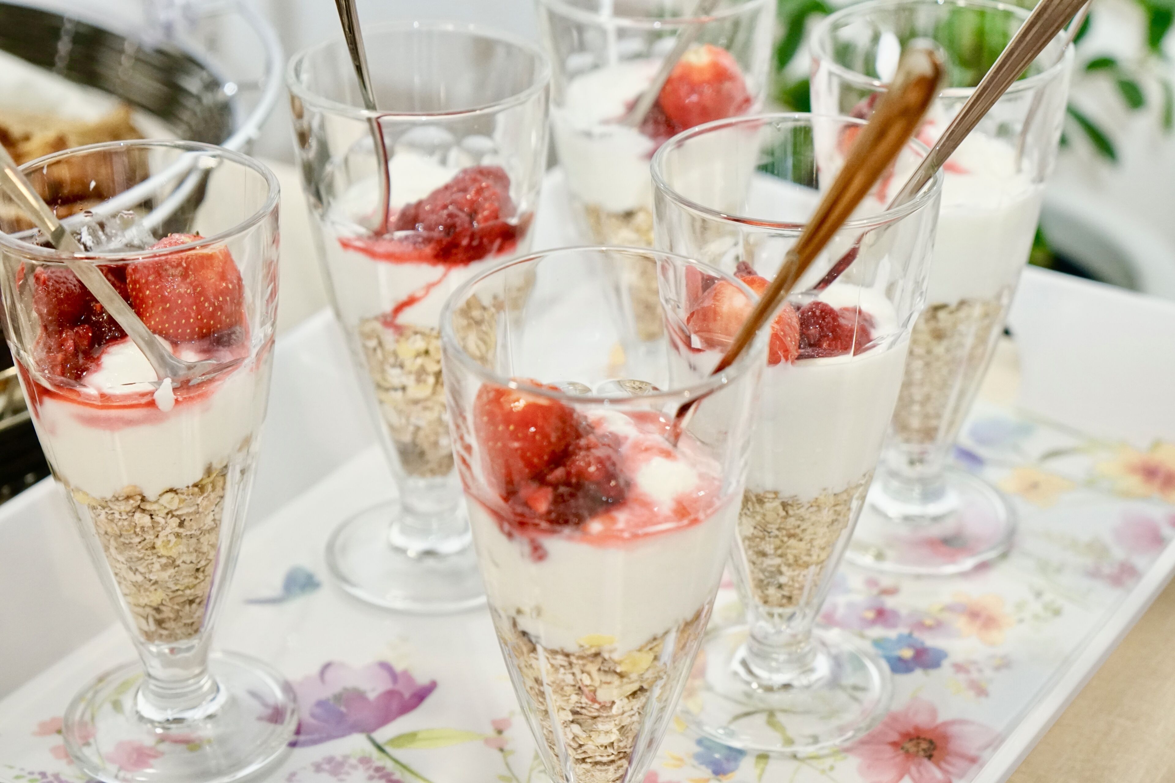 Un tavolo con diversi bicchieri di dessert stratificato, con yogurt, granola e fragole.