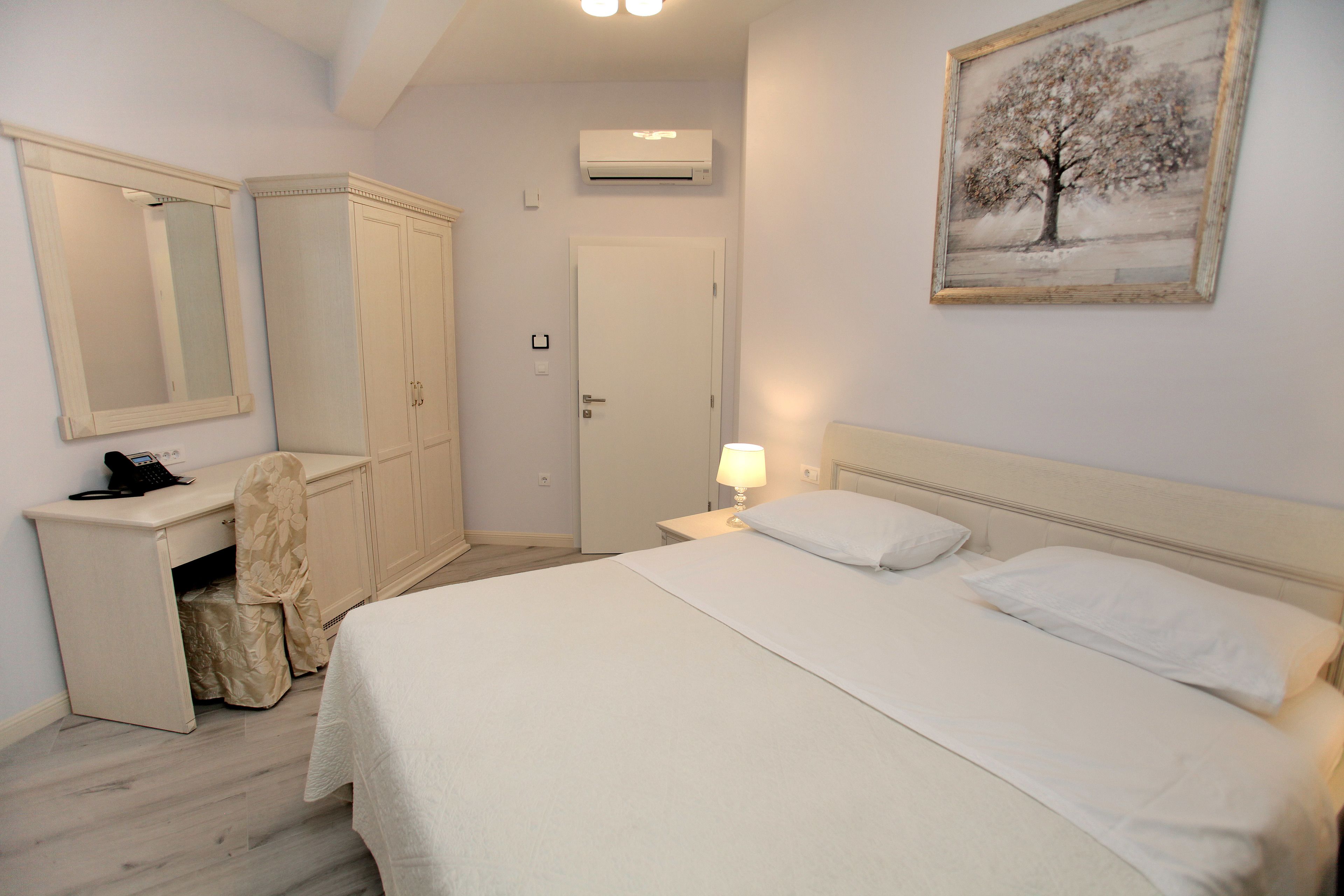 A bedroom with a bed, a desk, a wardrobe, and a painting on the wall.