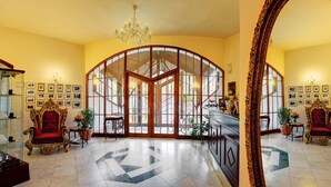 A grand lobby with a large arched glass door, ornate chairs, a chandelier, and a coffee station. - Hotel Bankov (Kosice)