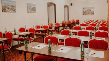 Un salón de conferencias con varias mesas y sillas rojas, cada una con una botella y un vaso encima.