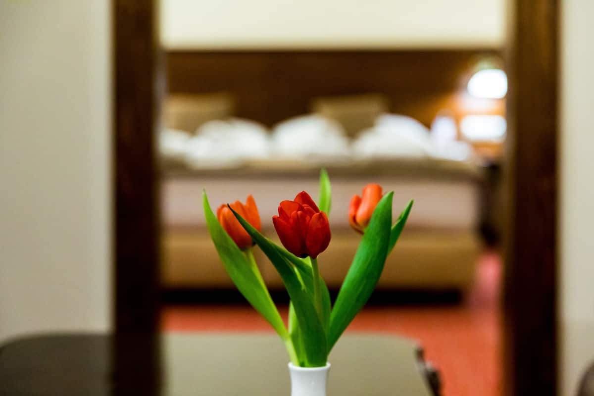 Un jarrón blanco con tulipanes rojos y anaranjados sobre una mesa en una habitación con fondo desenfocado.