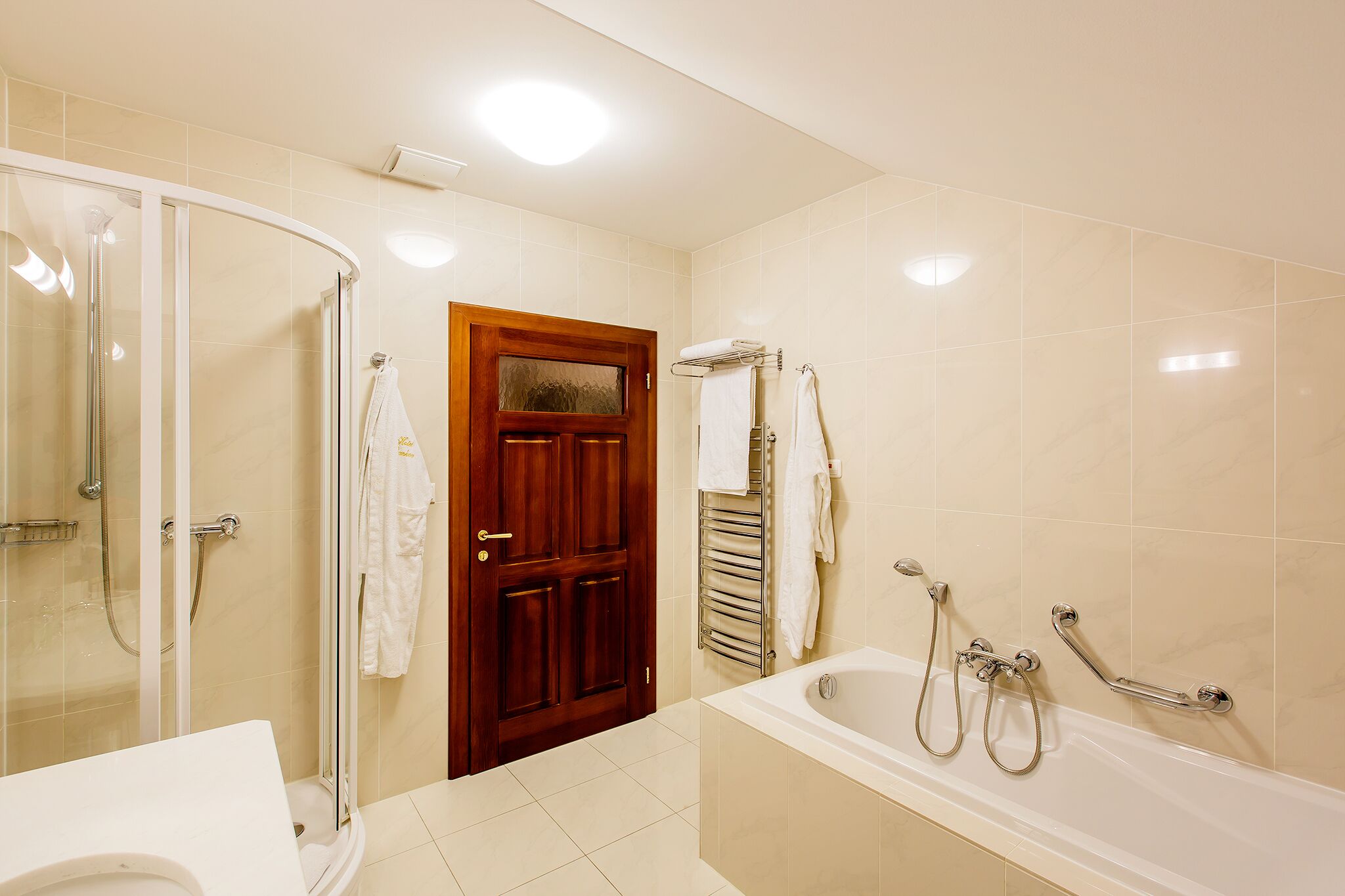 Un baño con ducha envuelta en vidrio, puerta de madera, bañera con barras de apoyo y un perchero para toallas.