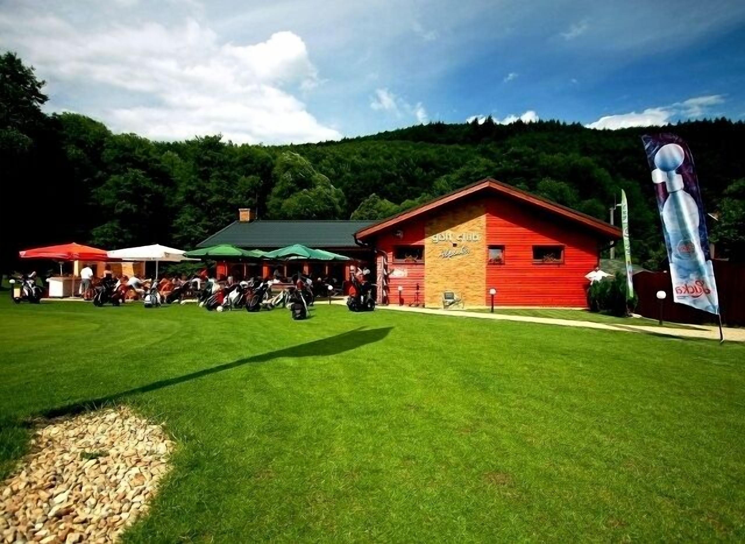A red building with a green roof, surrounded by a grassy area with people and golf carts.