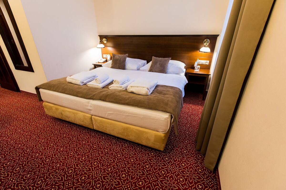 Una habitación de hotel con una cama grande, dos mesitas de noche con lámparas y una alfombra estampada.
