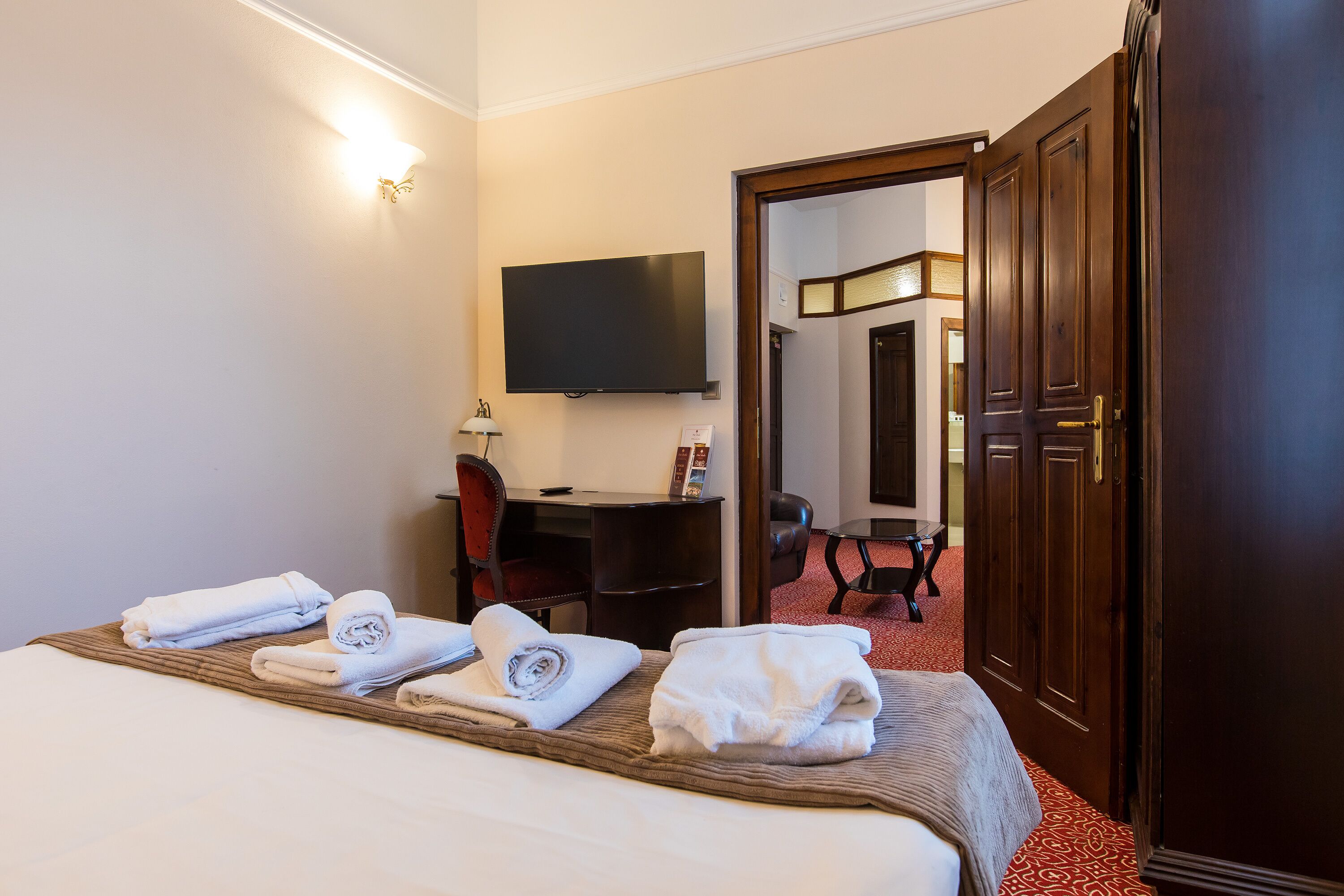 A hotel room with a bed, a desk, a chair, a TV, and a door leading to another room.