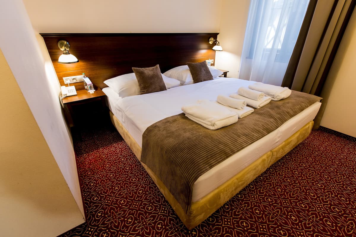 Una habitación de hotel con una cama grande, dos mesitas de noche con lámparas, un teléfono y una alfombra estampada.