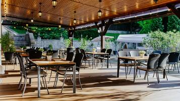 An outdoor patio with tables and chairs, wooden ceiling, and hanging lights.