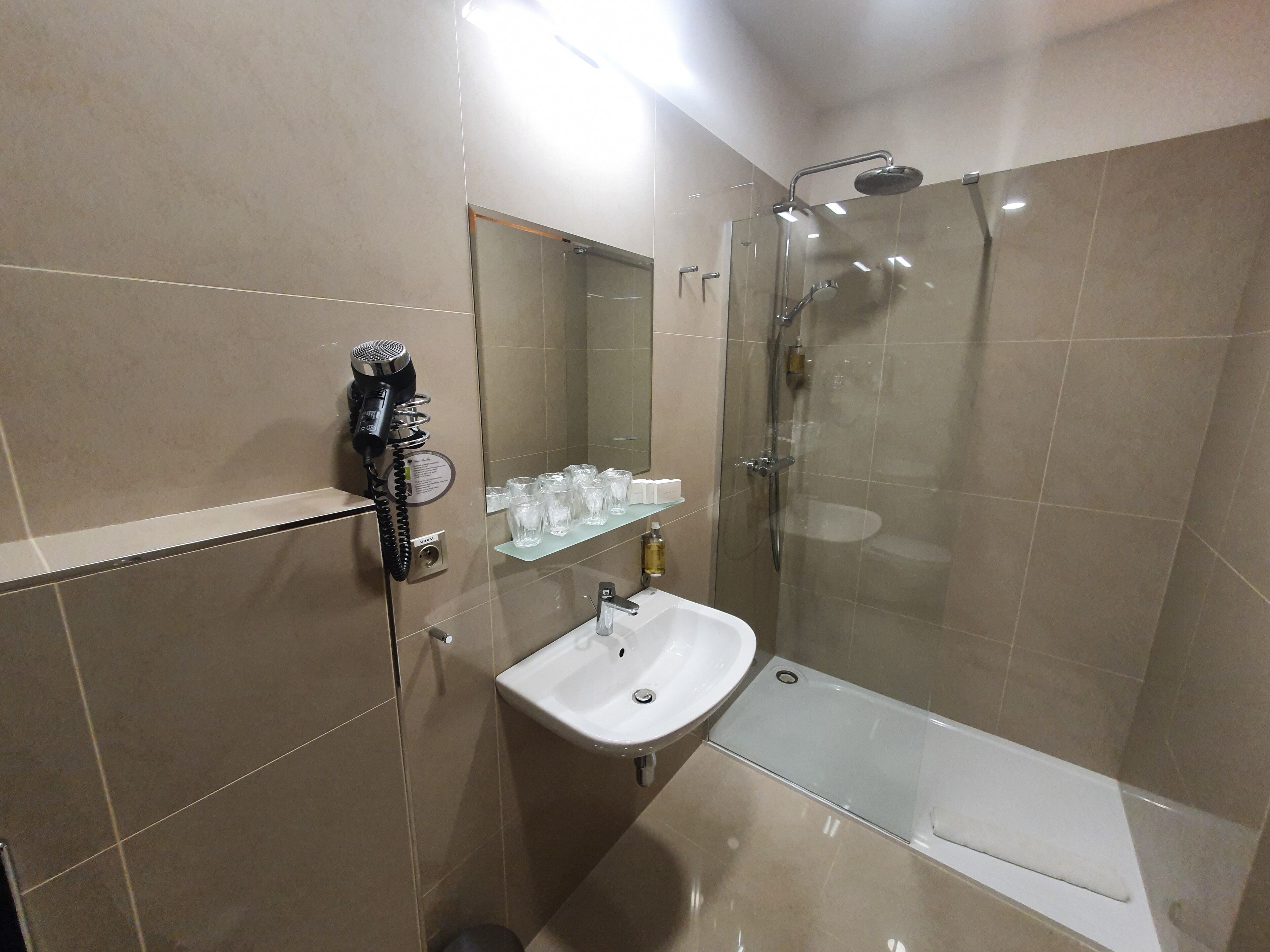 A modern bathroom with a glass-enclosed shower, a sink, and a hairdryer on a wall-mounted rack.