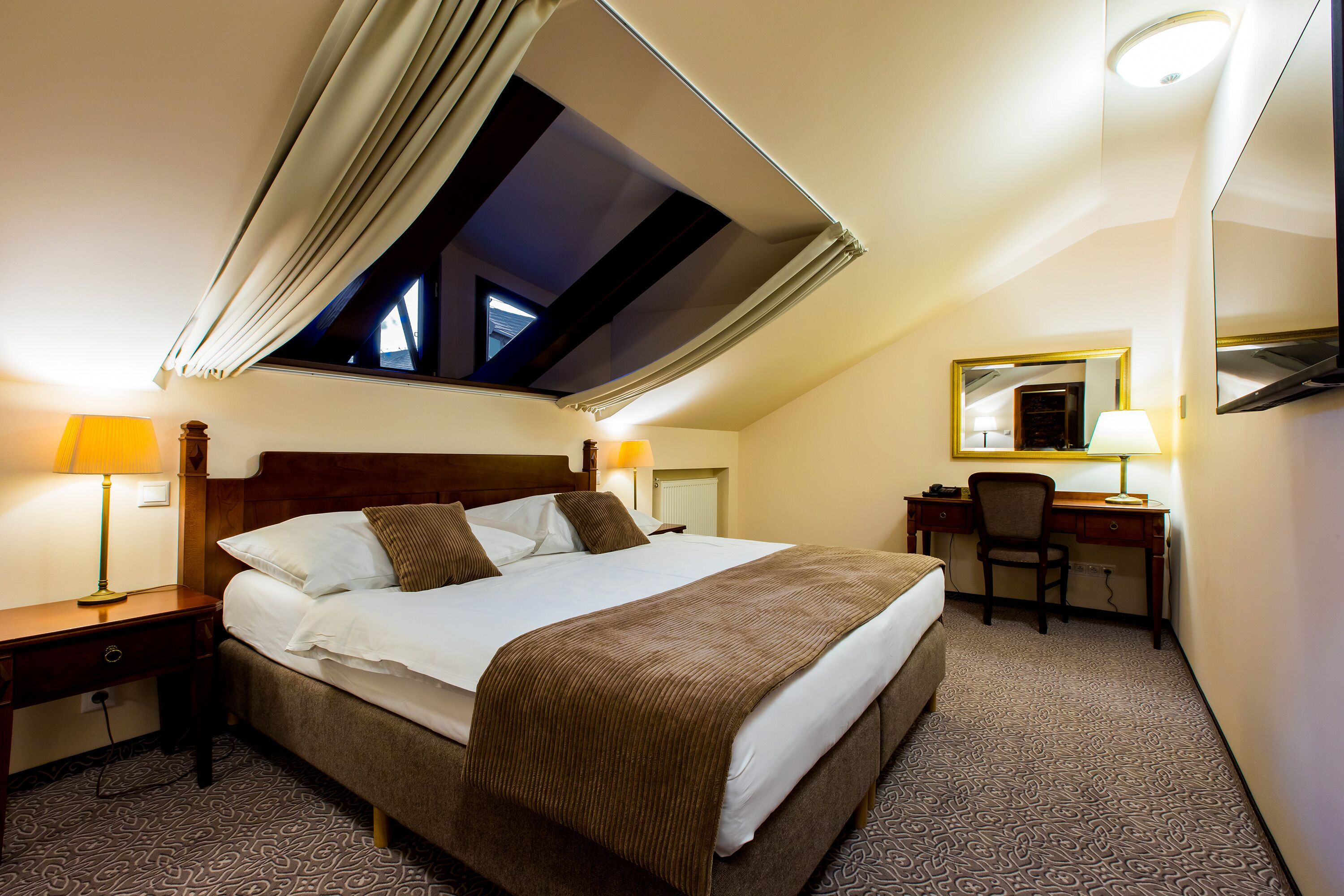 Ein Hotelzimmer mit einem großen Bett, einem Schreibtisch, einem Stuhl, einer Schreibtischlampe und einem Fenster mit Vorhängen.
