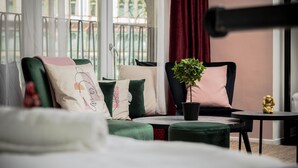 A cozy room with a green sofa set, a small table with a plant, and a view of a balcony with red curtains. - Maverick Downtown (Budapest)
