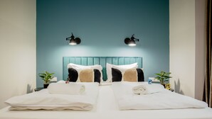 A hotel room with a teal-colored headboard, two bedside tables with lamps, a bed with white linens and towels, and two potted plants. - Maverick Downtown (Budapest)