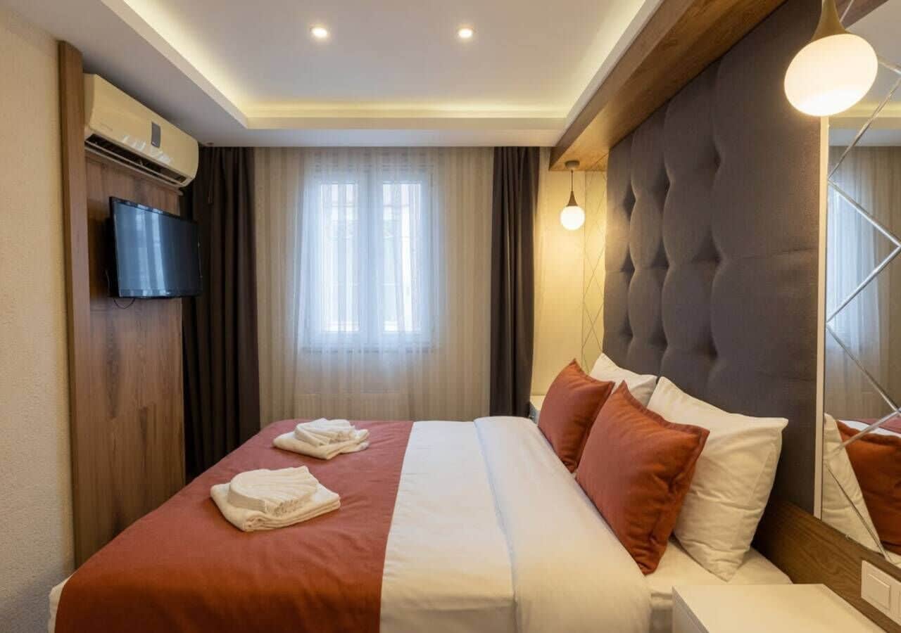 Een hotelkamer met een bed, een flatscreen televisie, een airconditioning en een groot raam met gordijnen.