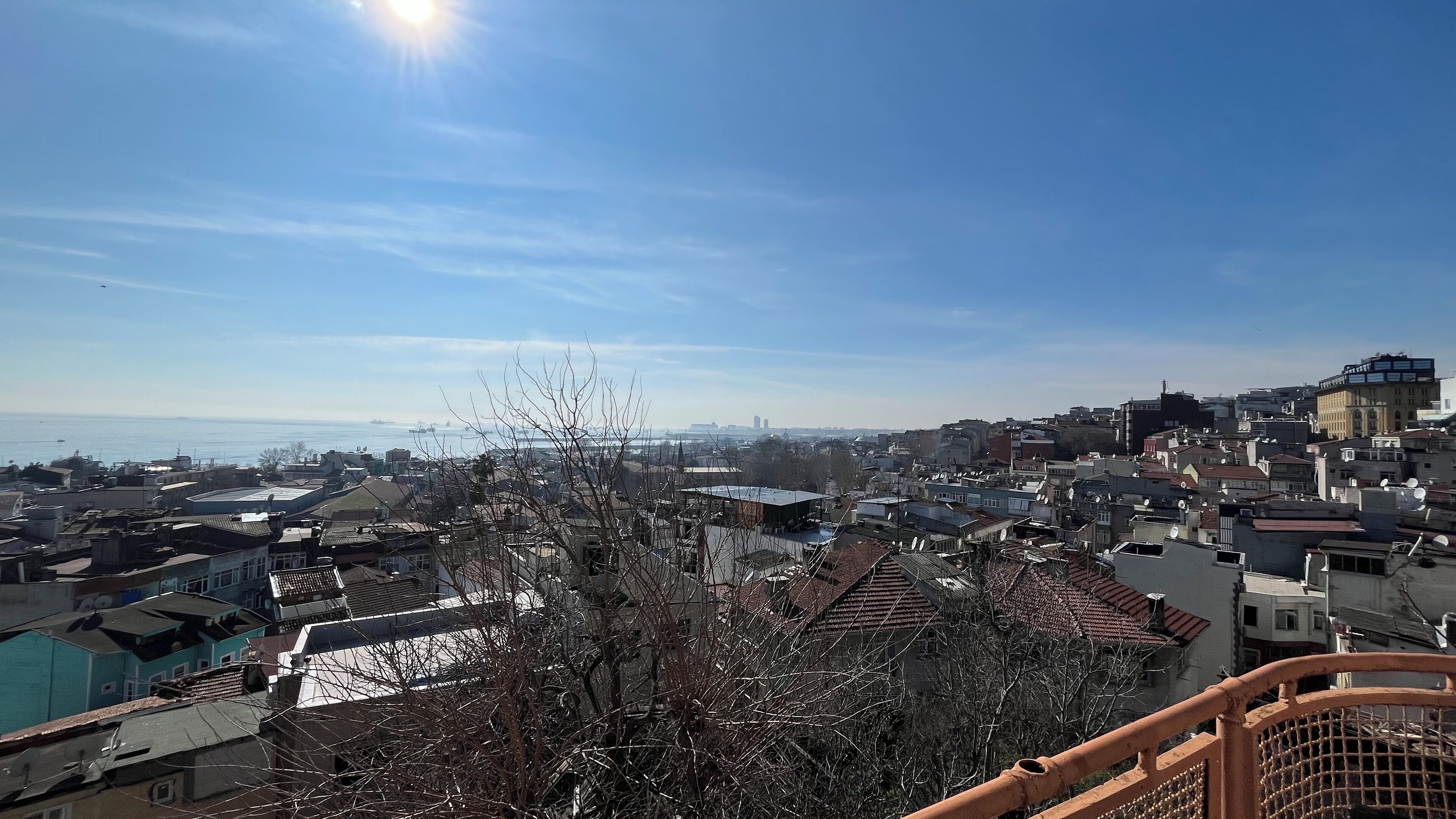 Paesaggio urbano con edifici residenziali e commerciali, cielo sereno e un corpo d'acqua all'orizzonte.