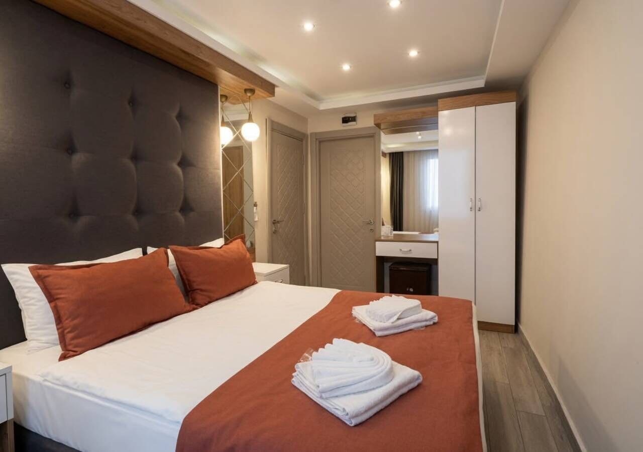 Habitació d'hotel amb un llit gran, un panell de capçalera de fusta, una tauleta de nit, un mirall i un armari.