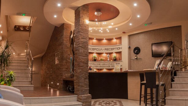 A reception area with a reception desk, a clock, and a staircase leading to upper floors. - Vigor Hotel (Novi Sad)