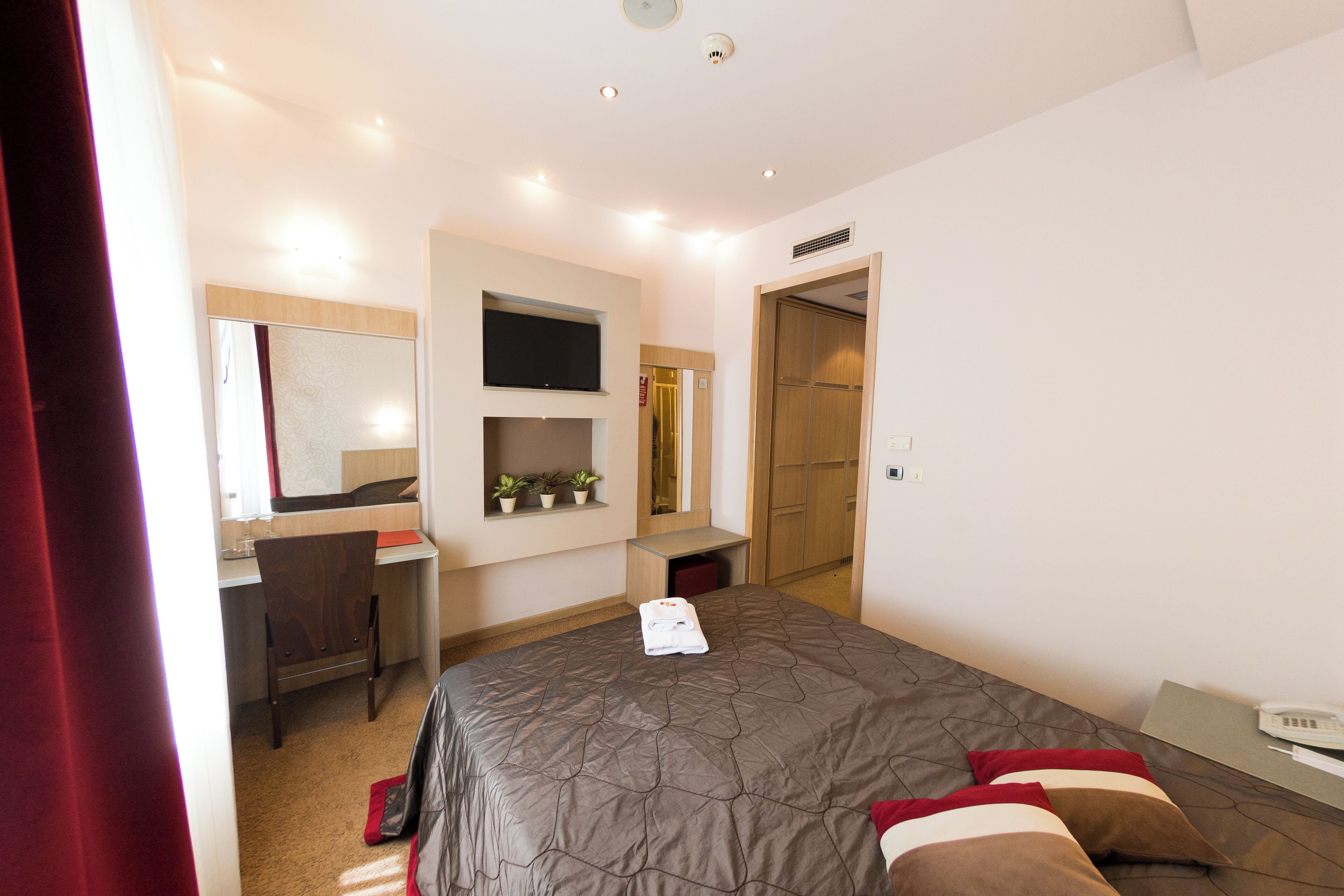 A modern hotel room with a large bed, a desk, a flat-screen TV, and a wardrobe.