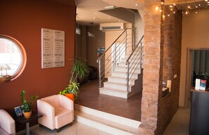 A hotel lobby with a staircase, a reception desk, and a seating area with plants.
